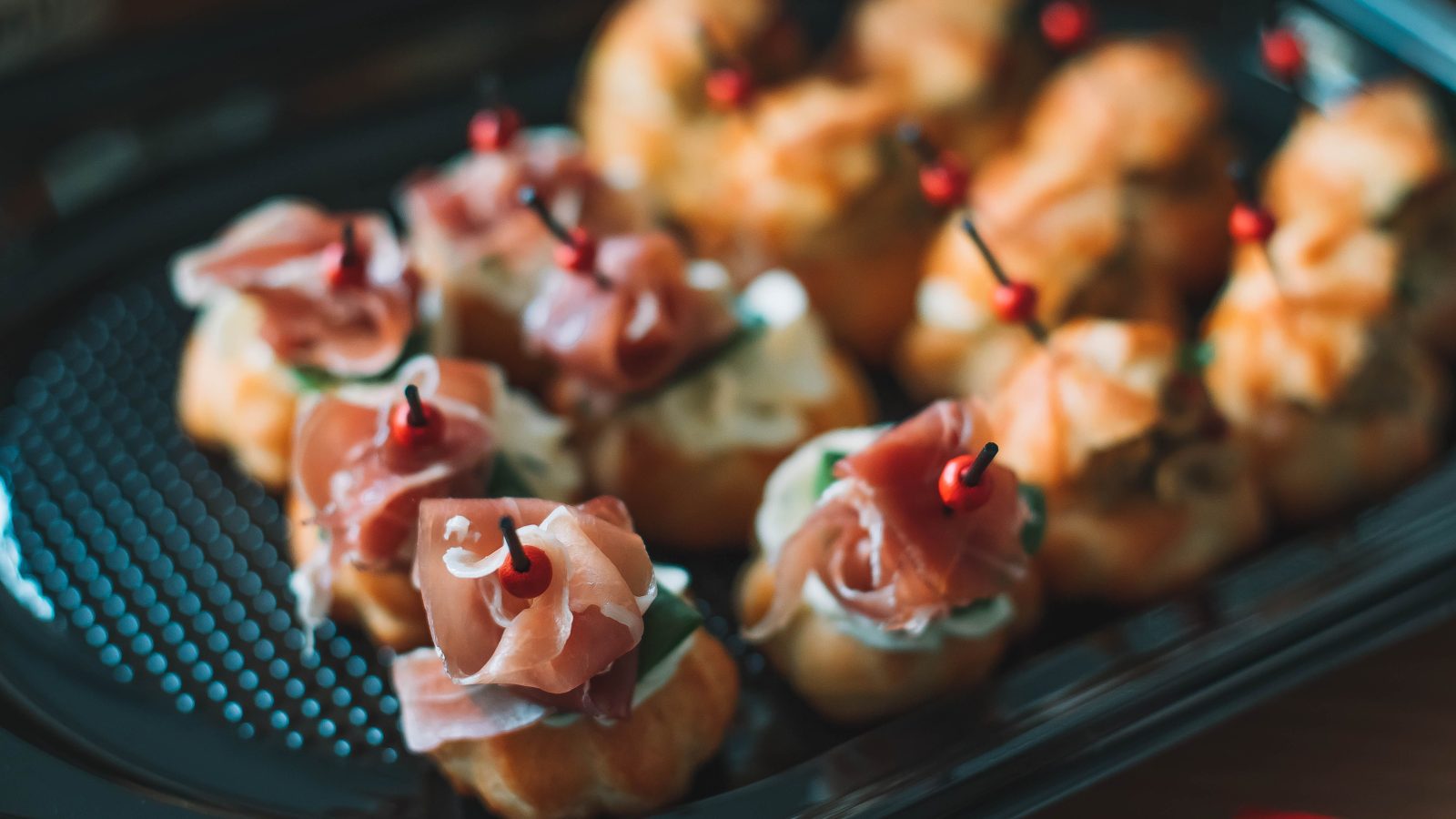 Choux salés garnis de jambon cru sur un plateau, présentés en pièces pour l'apéritif