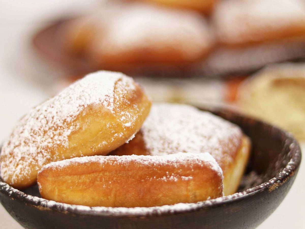 Beignets ronds et dores presentes dans un bol, roules dans le sucre