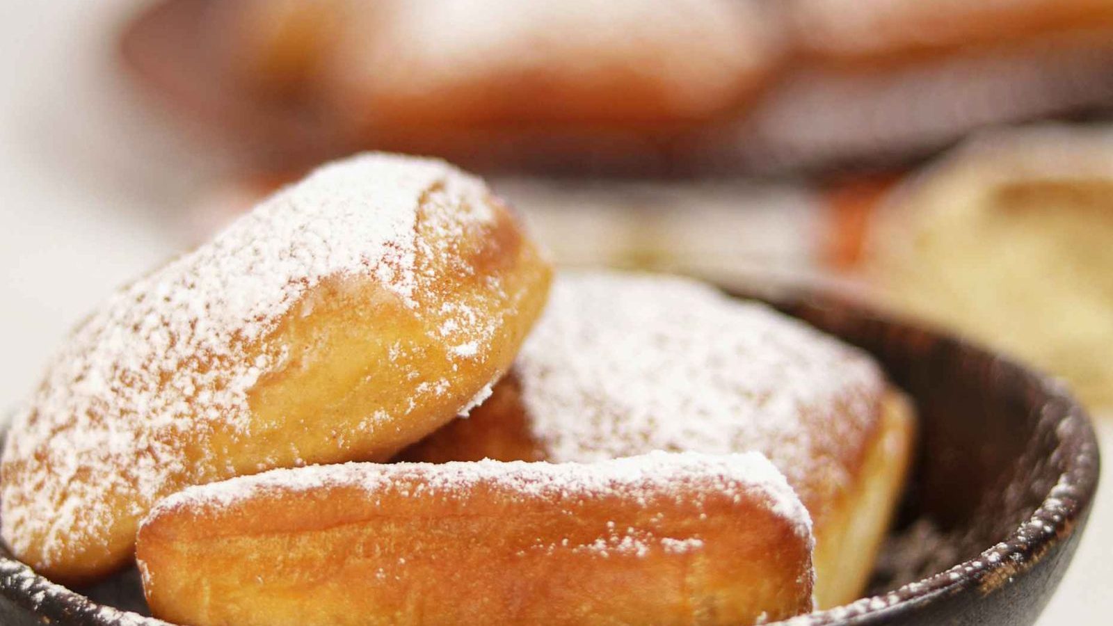 Beignets ronds et dores presentes dans un bol, roules dans le sucre