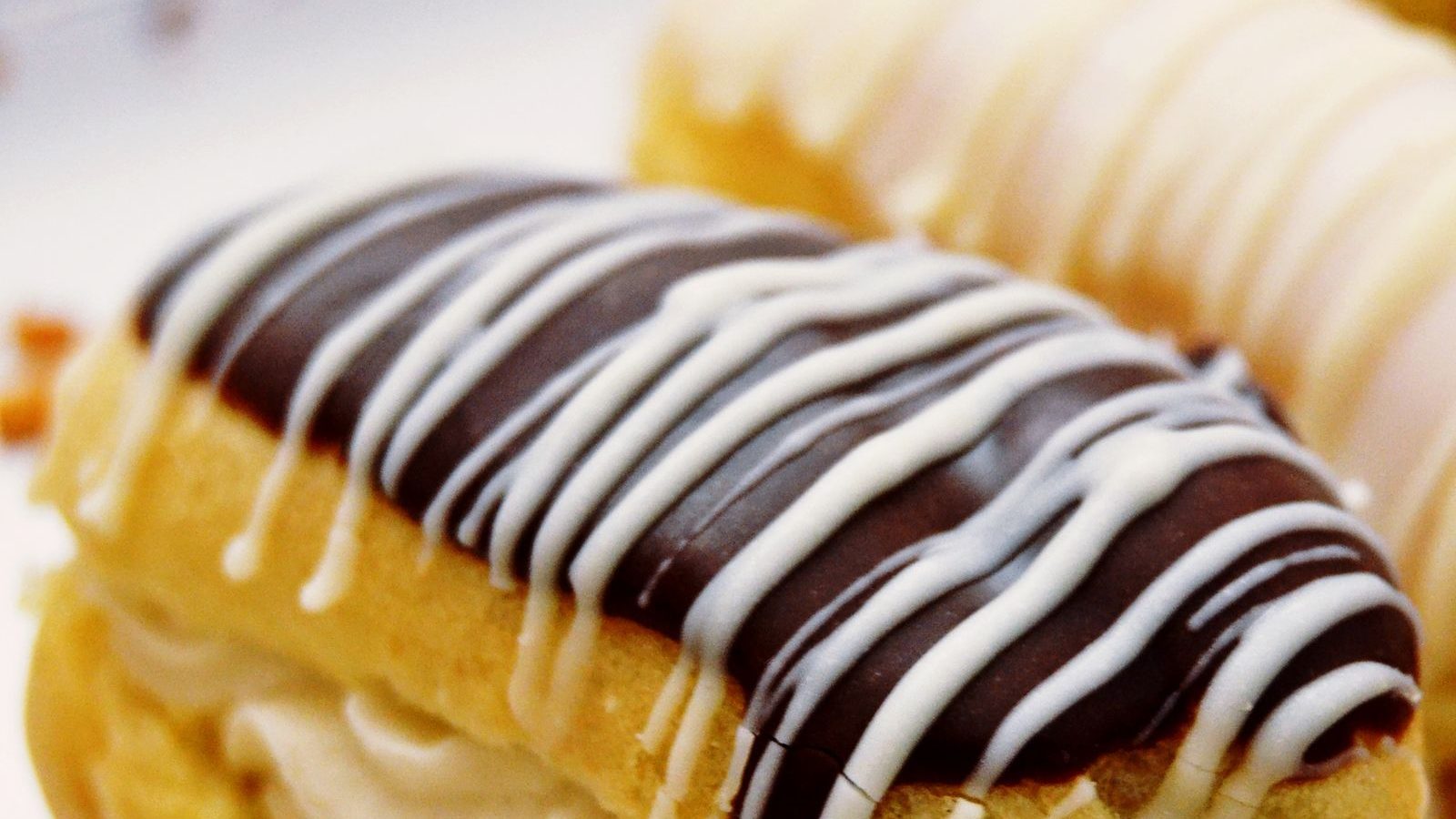 Eclair coupe montrant un glacage au fondant chocolat brillant, decore de filets de fondant blanc