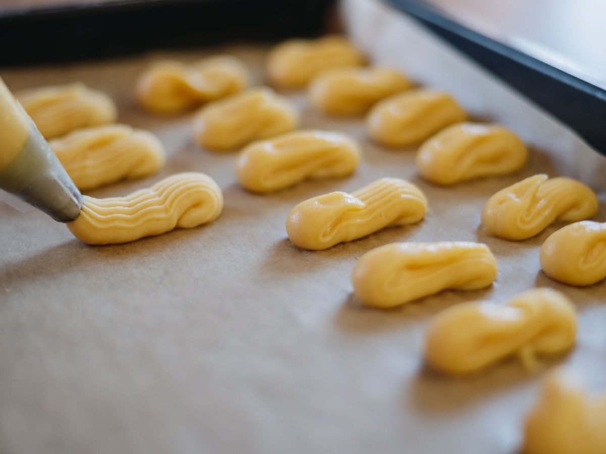 Pâte à choux crue dressée à la poche à douille sur une plaque recouverte de papier cuisson