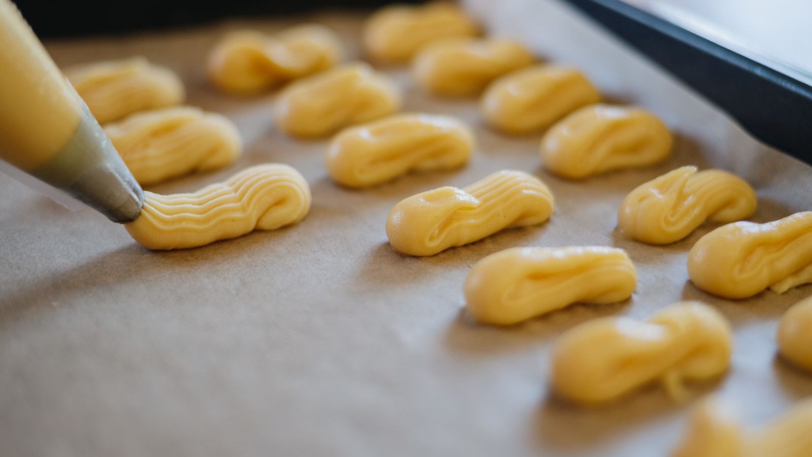 Pâte à choux crue dressée à la poche à douille sur une plaque recouverte de papier cuisson