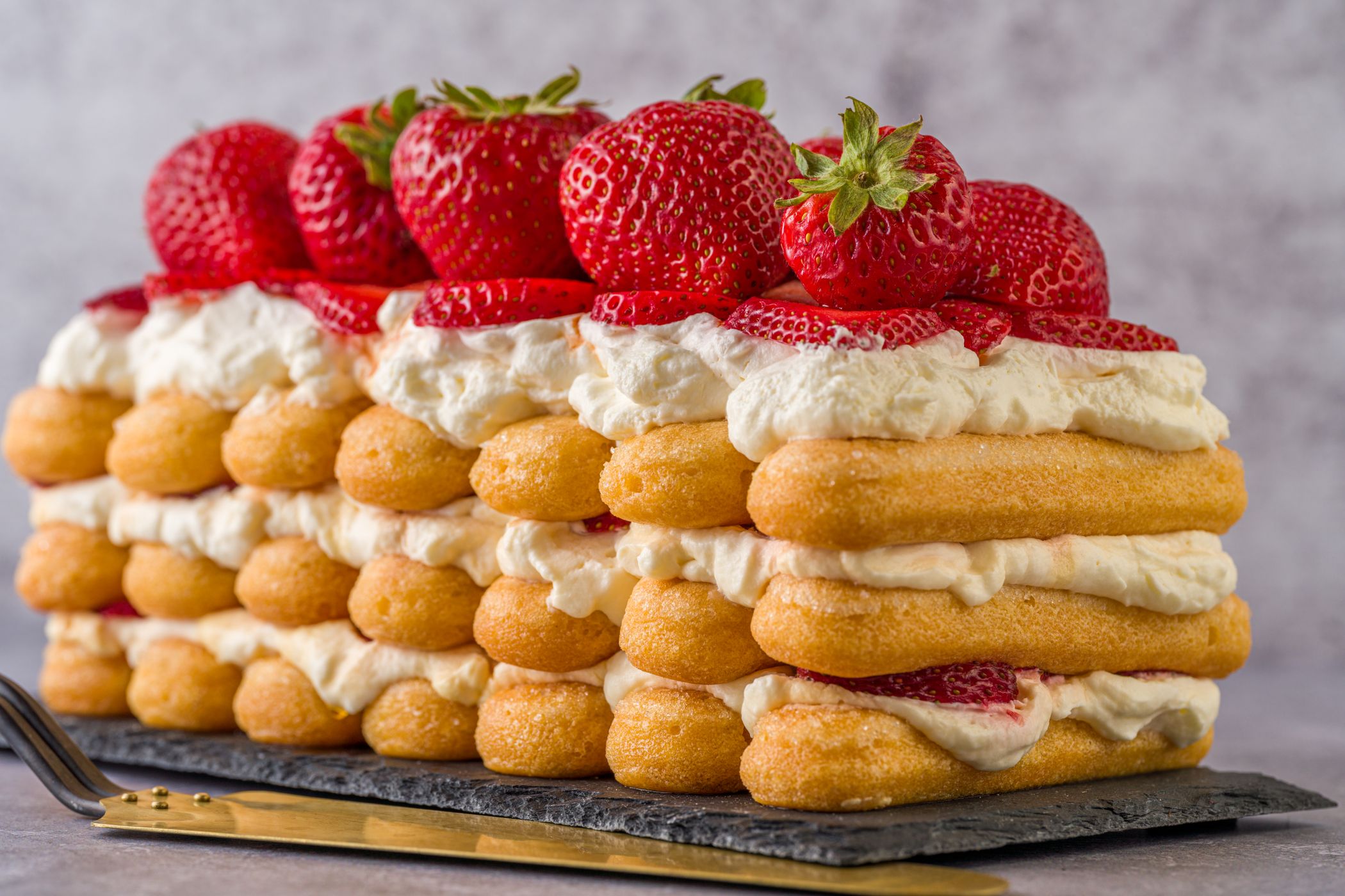 Biscuits cuillère disposés en couches avec de la crème fouettée et des fraises fraîches, façon charlotte aux fraises